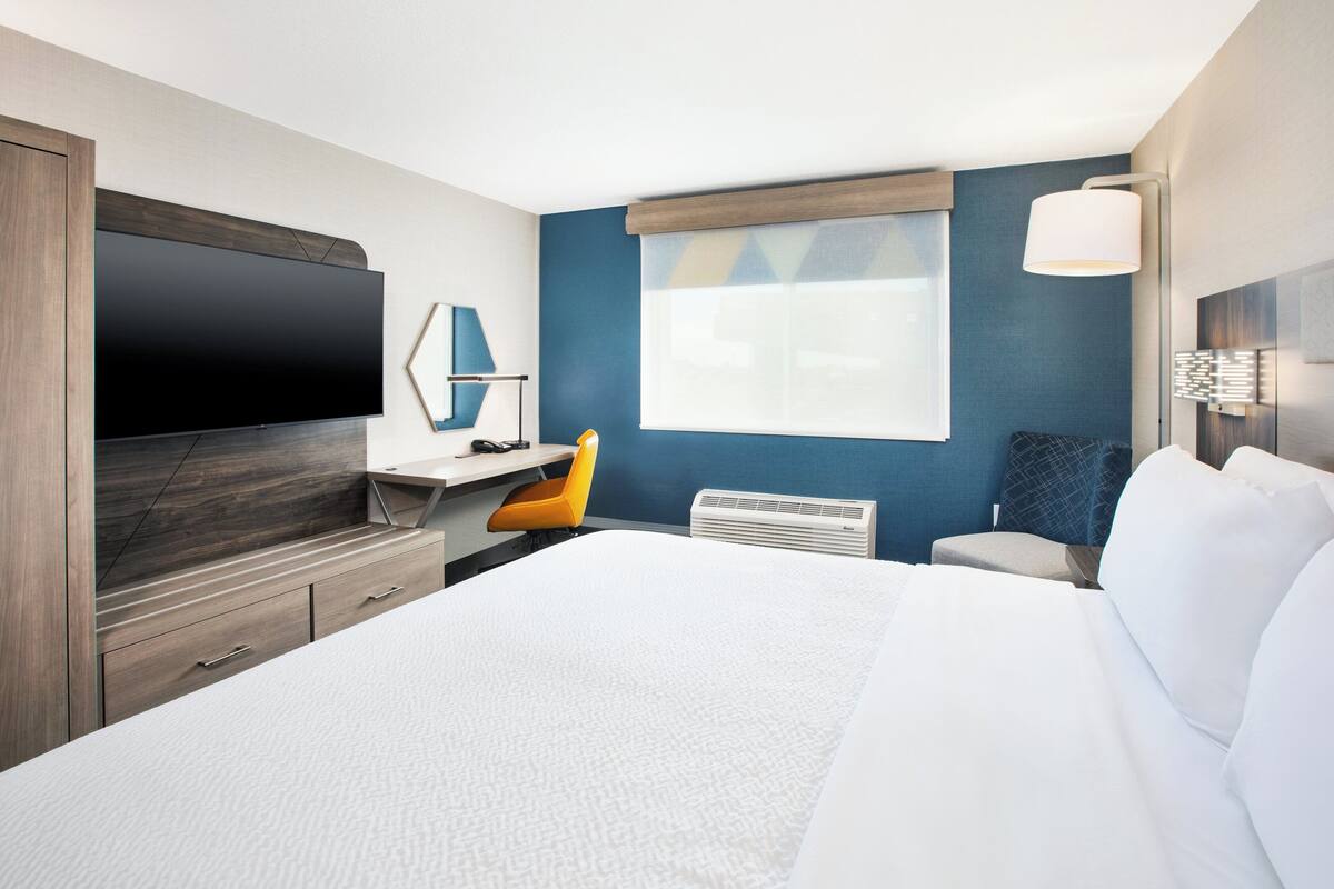 A modern hotel room with a large bed, a flat-screen TV, a desk with a chair, and a window with a view.