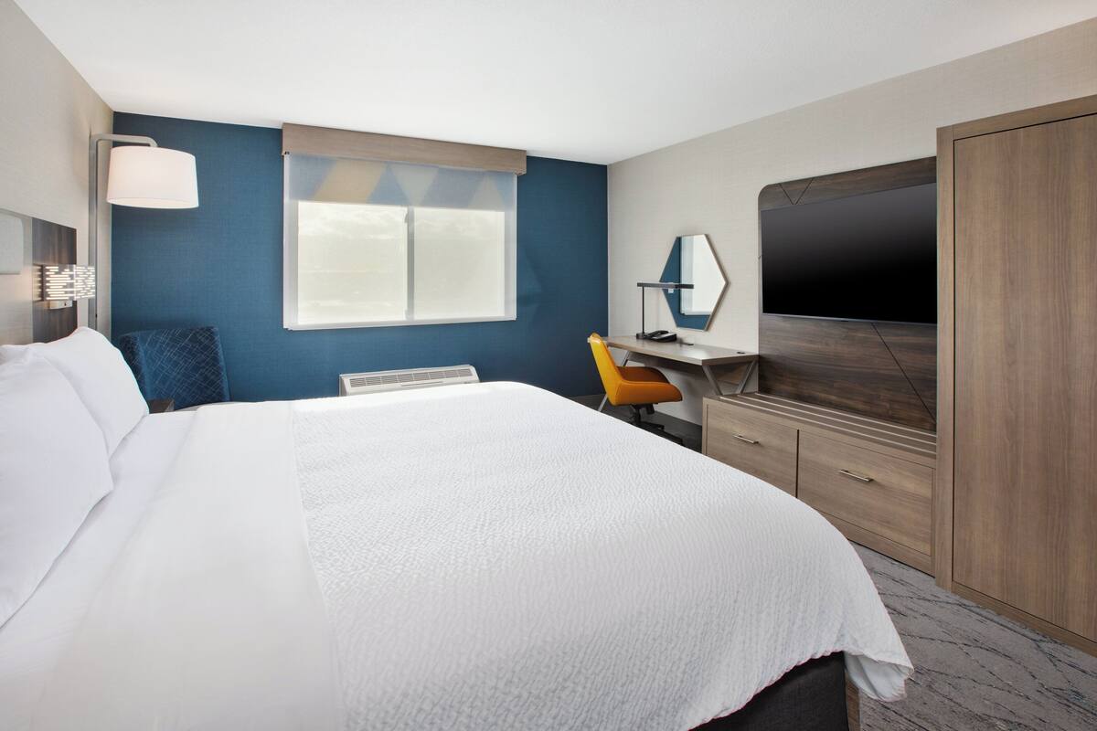A hotel room with a large bed, a desk with a chair, a TV, and a wardrobe.