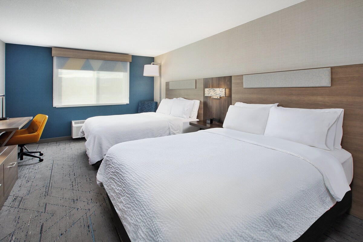 A hotel room with two beds, a desk, and a chair.