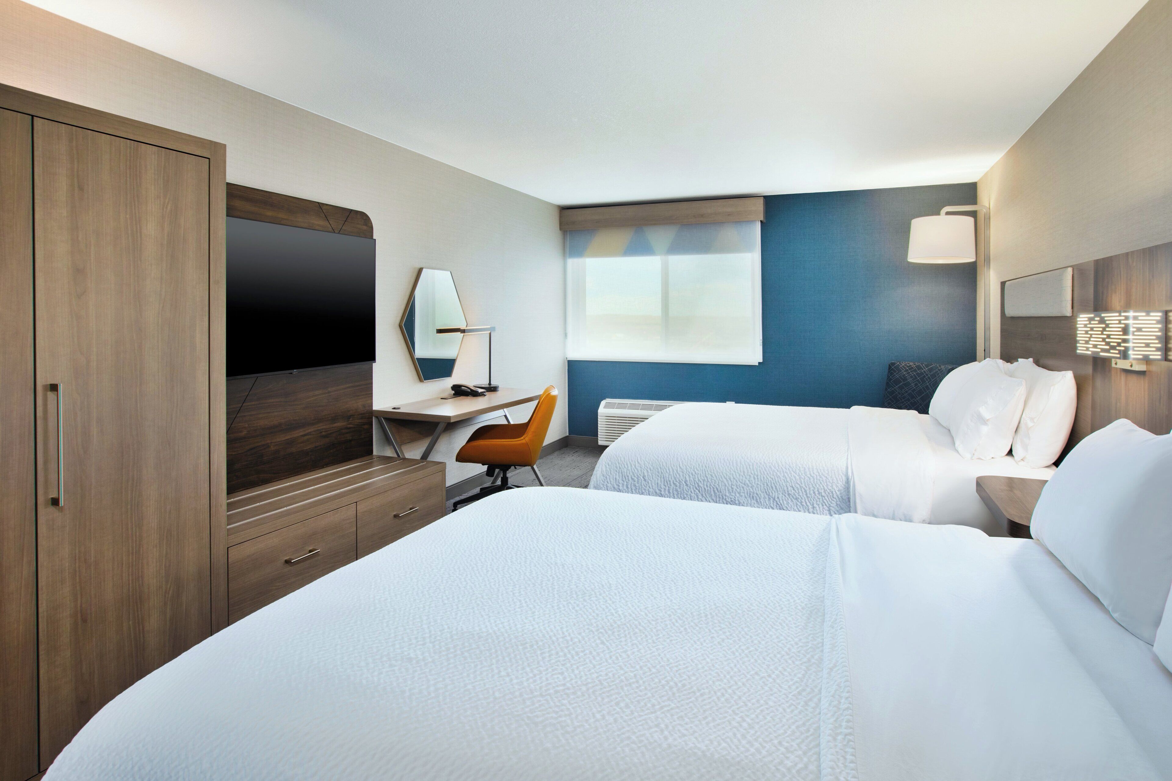 A hotel room with two beds, a desk, a chair, a TV, and a large window.