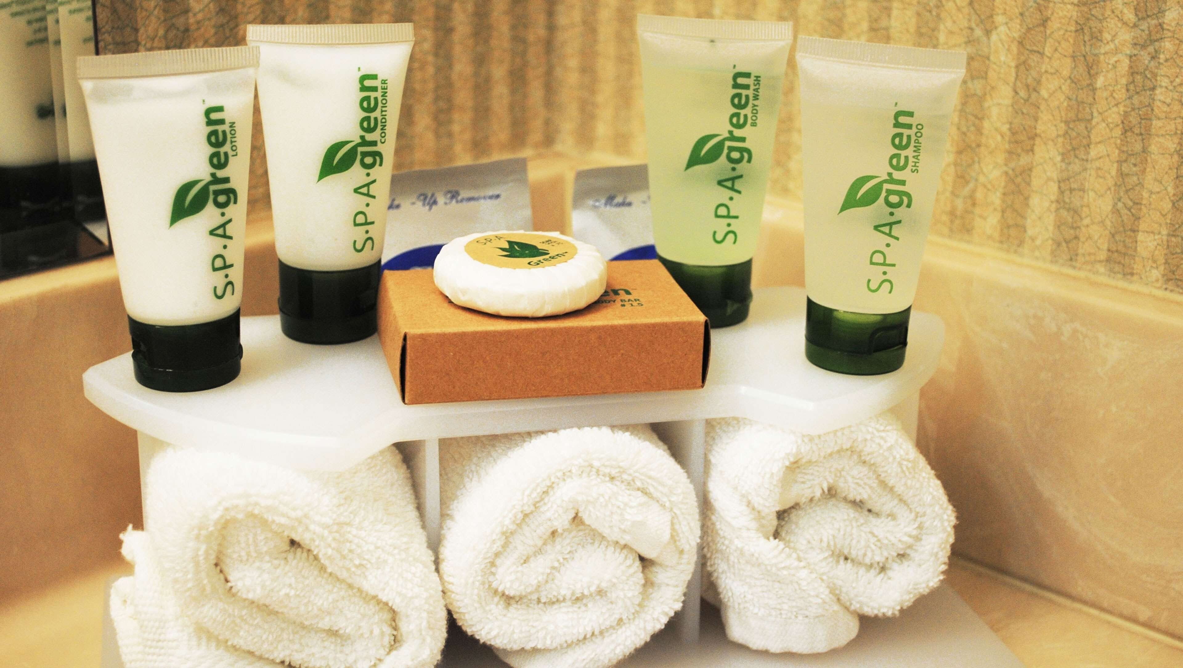 A bathroom vanity with toiletries including lotion, conditioner, body wash, and shampoo, along with neatly rolled towels.