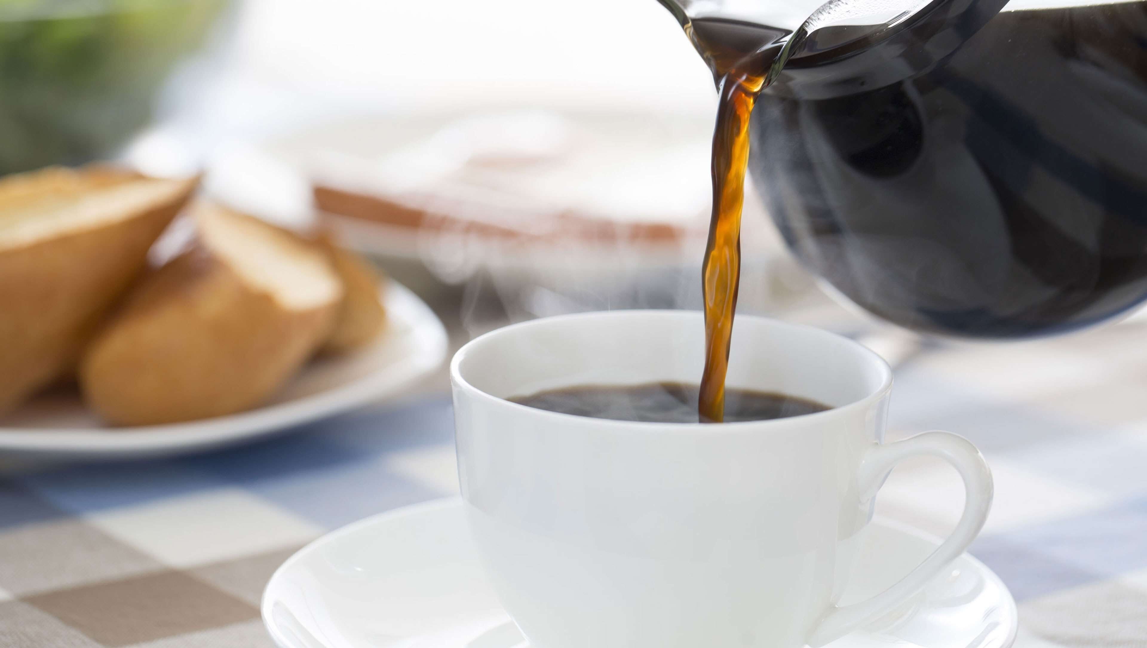 A cup of coffee being poured from a black coffee pot.