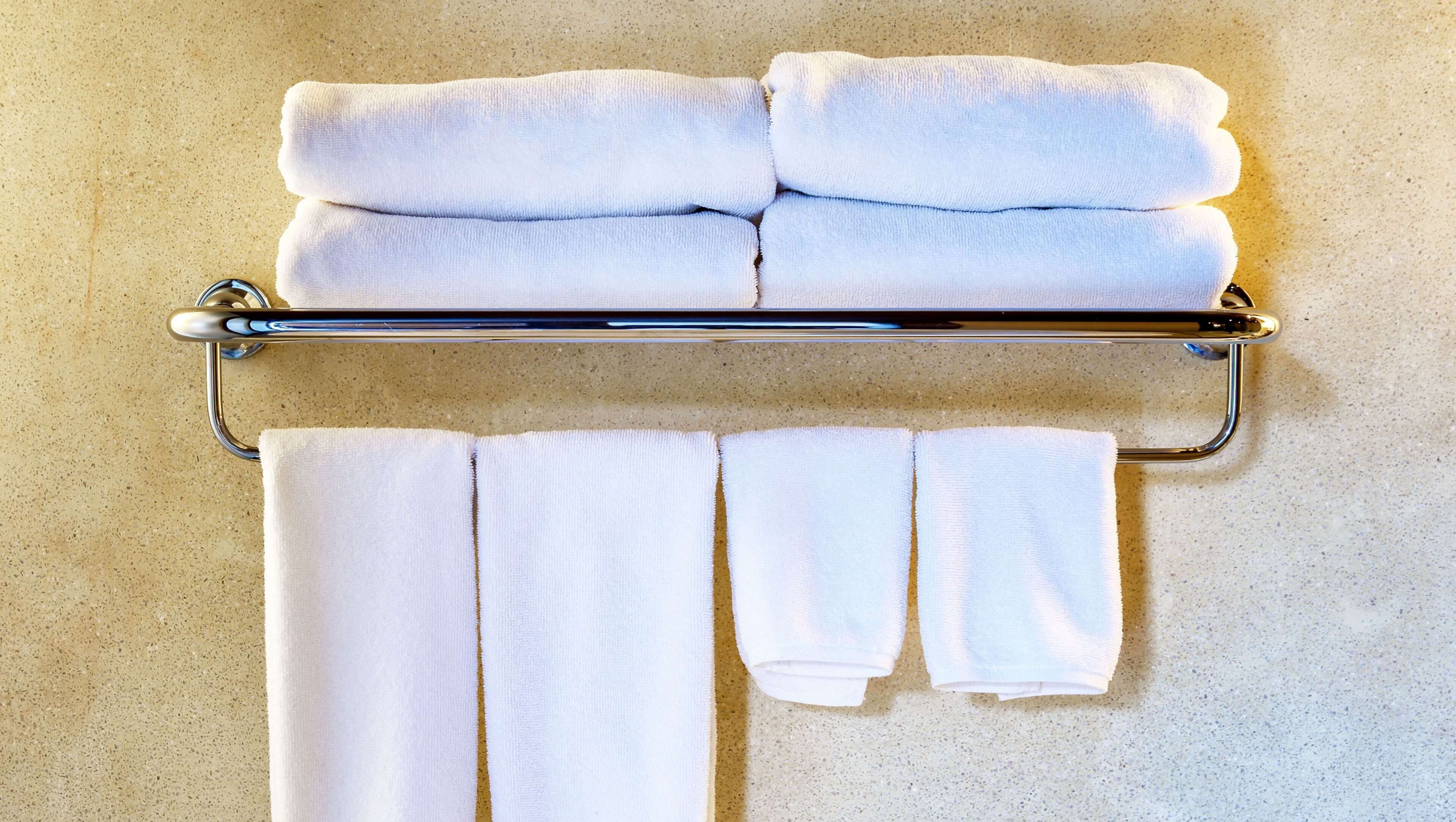 A metal towel rack with four neatly folded white towels and three hanging towels against a speckled wall.