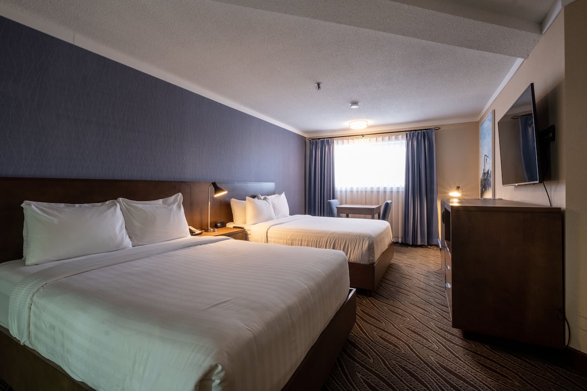 Ett hotellrum med två sängar, ett skrivbord, en stol, en TV och ett fönster med gardiner.
