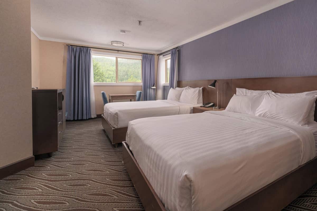 Ett hotellrum med två sängar, ett skrivbord, en stol och ett fönster med gardiner.