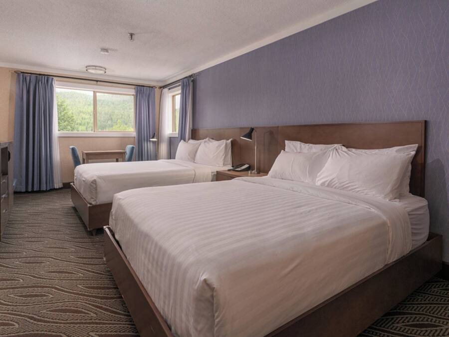 A hotel room with two beds, a desk, a chair, and a window with curtains.