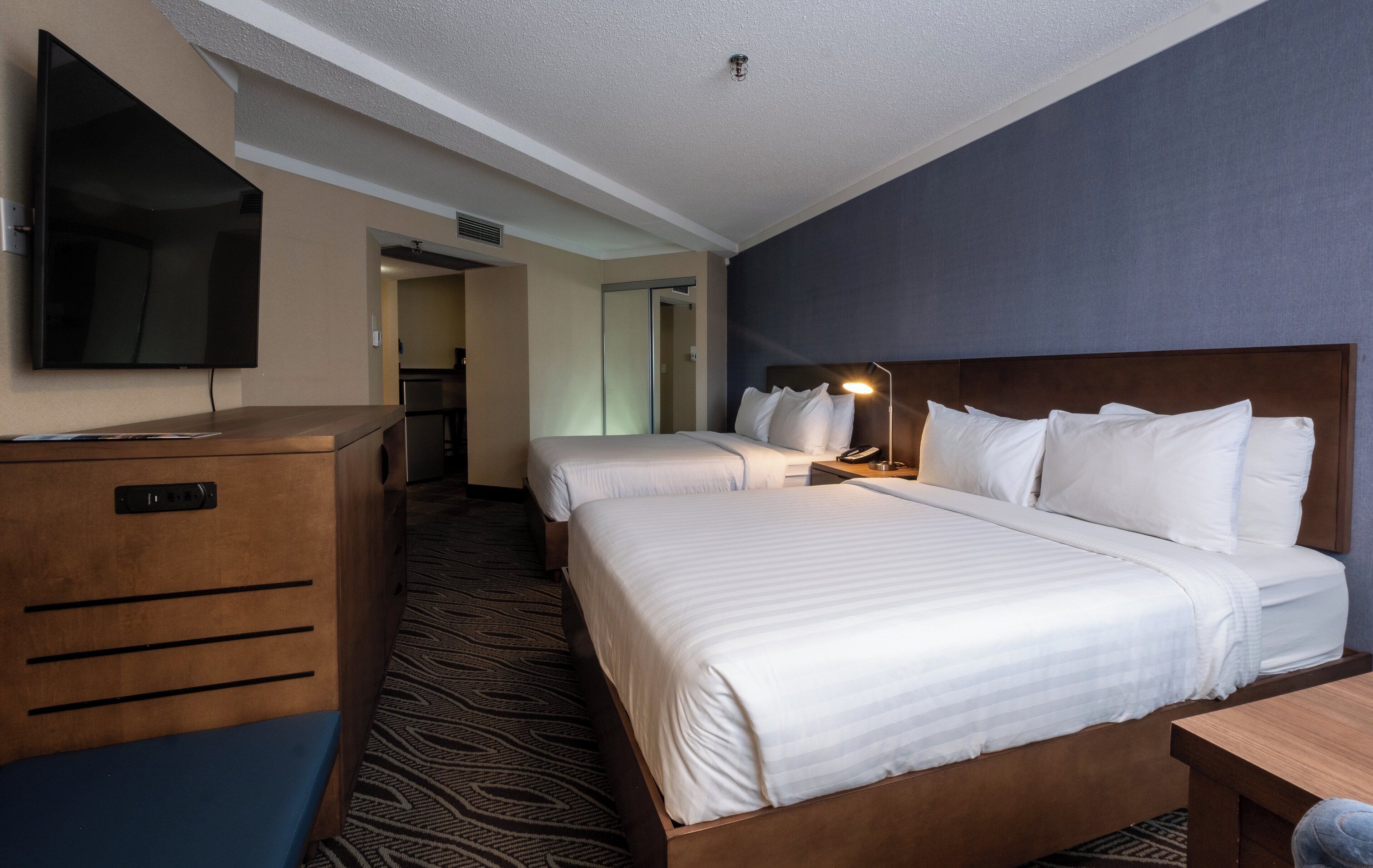 A hotel room with two beds, a TV mounted on the wall, a desk, and a wardrobe.