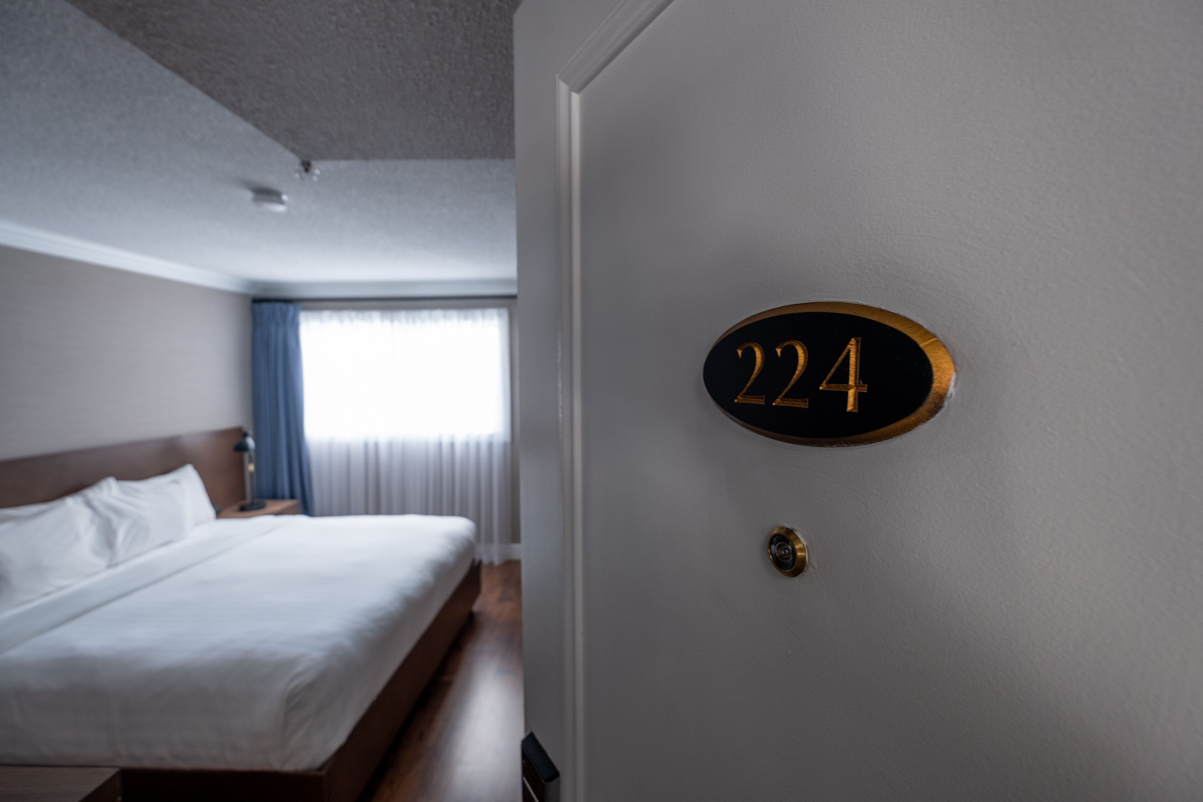 Habitación de hotel con cama, una puerta con el número 224 y una ventana con cortinas.