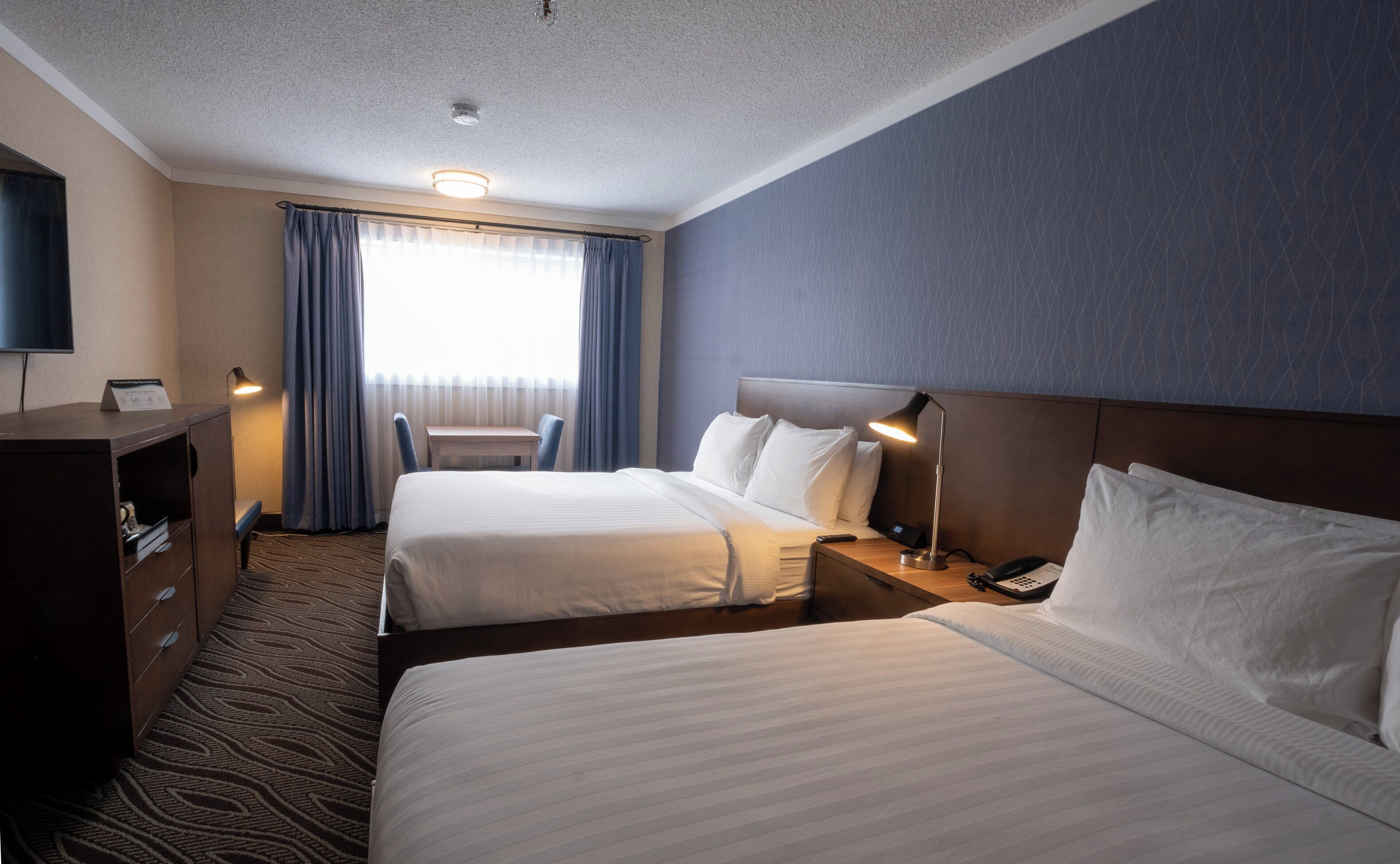 A hotel room with two beds, a desk, a chair, a TV, and a window with curtains.