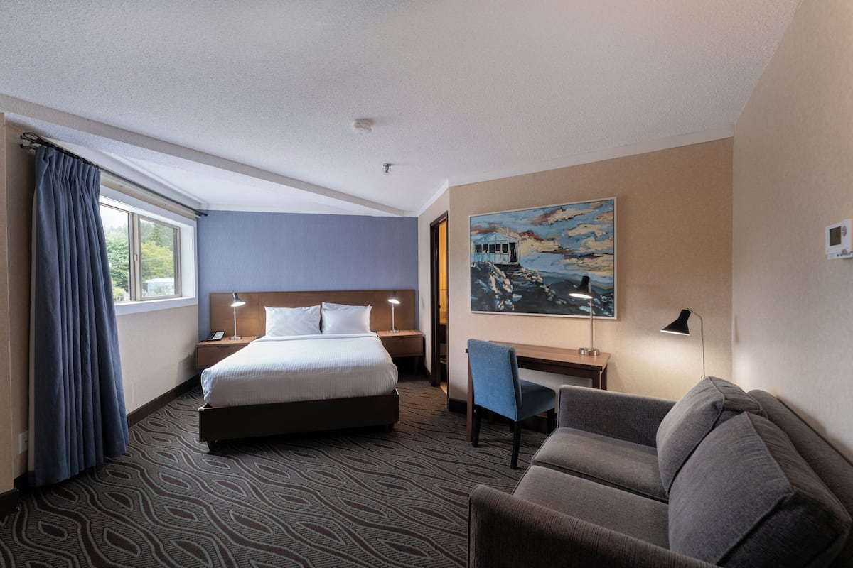 Ett hotellrum med en säng, ett skrivbord, en stol och en tavla på väggen.