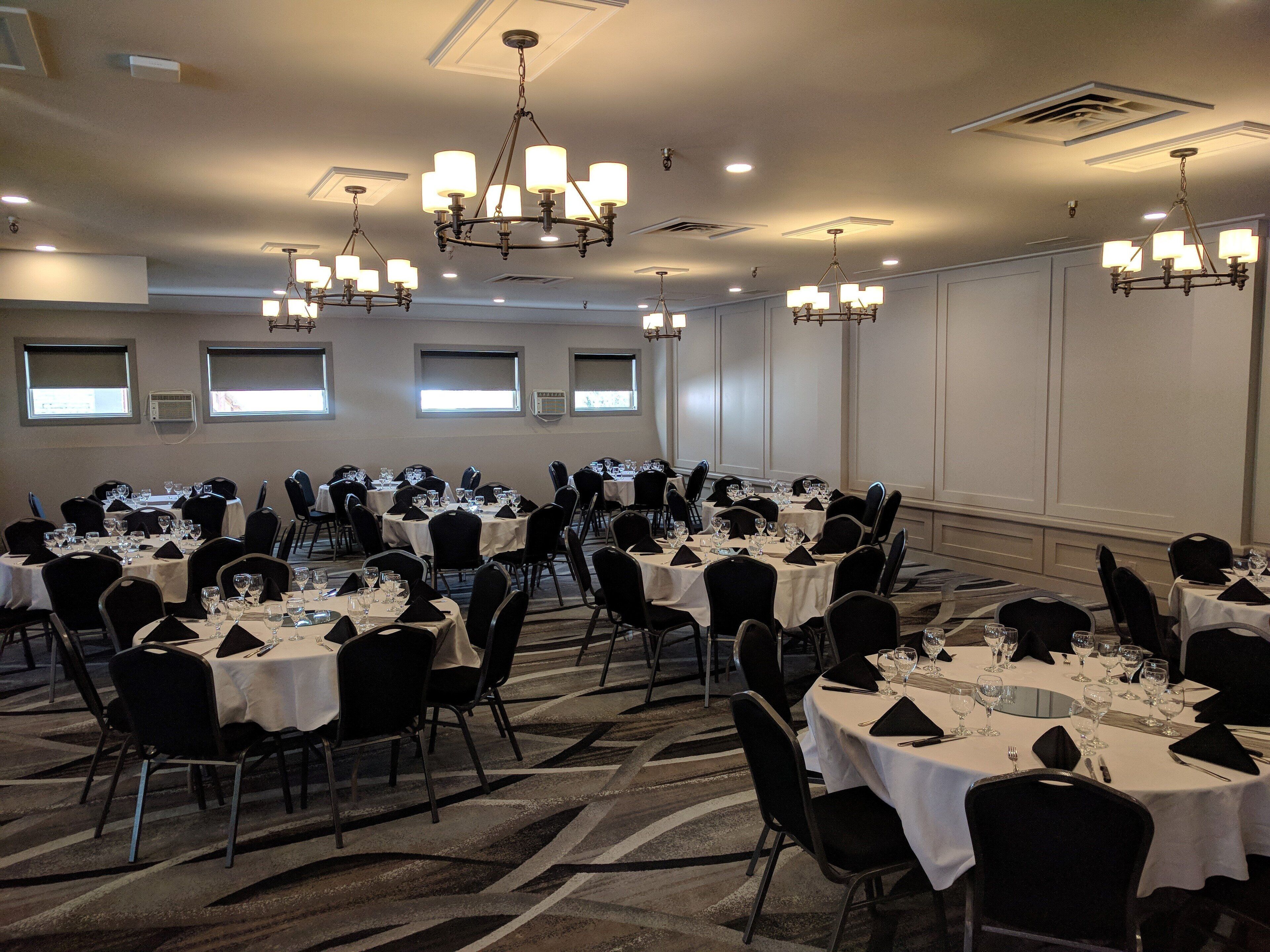 Une salle de banquet avec de nombreuses tables rondes, des chaises noires et des lustres.