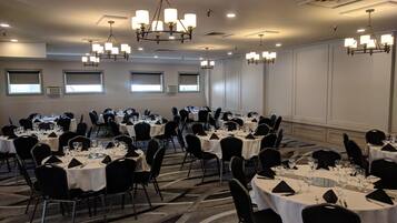 Une salle de banquet avec de nombreuses tables rondes, des chaises noires et des lustres.