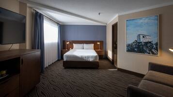 Habitación de hotel con una cama grande, un televisor de pantalla plana, un aparador de madera, un cuadro en la pared y una alfombra estampada.