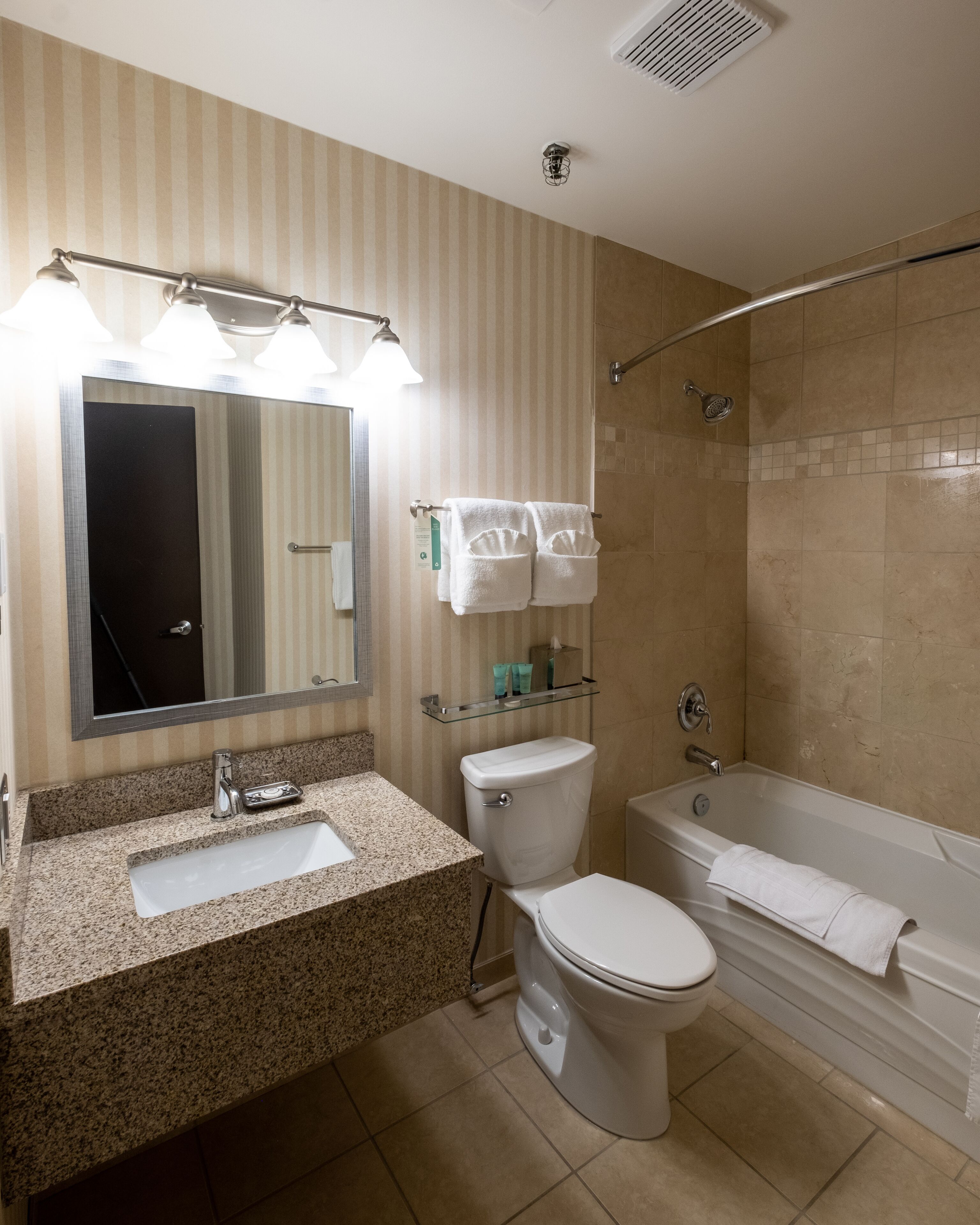 Un baño con lavamanos, inodoro y bañera. Hay un cabezal de ducha y un perchero con toallas.