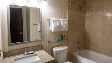 Un baño con lavamanos, inodoro y bañera. Hay un cabezal de ducha y un perchero con toallas.