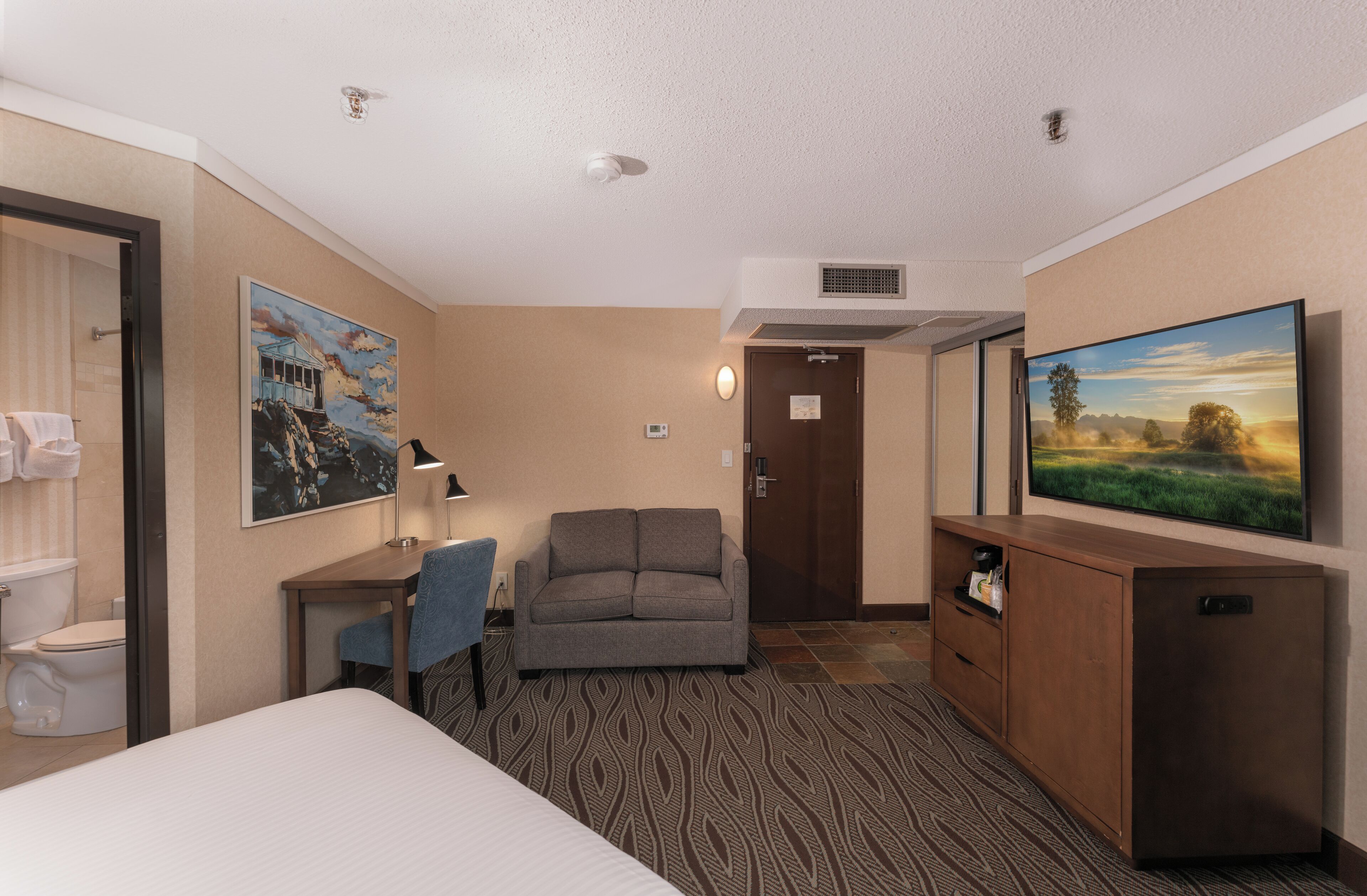 A hotel room with a bed, a desk, a sofa, a TV, and a bathroom.