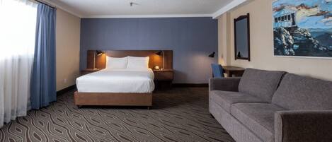 A hotel room with a large bed, a sofa, a painting, and a patterned carpet.