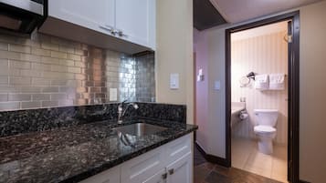 A modern kitchen with granite countertops, a stainless steel sink, and white cabinetry.