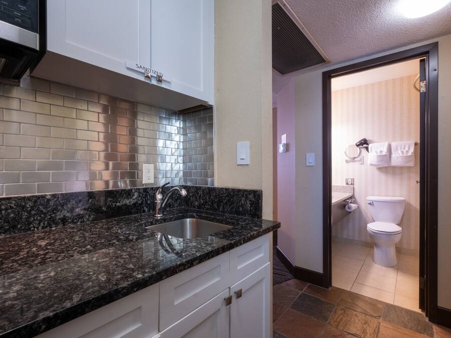 A modern kitchen with granite countertops, a stainless steel sink, and white cabinetry.