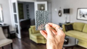 A hand holding a card with names, in a living room with a green sofa, a coffee table, and a TV.