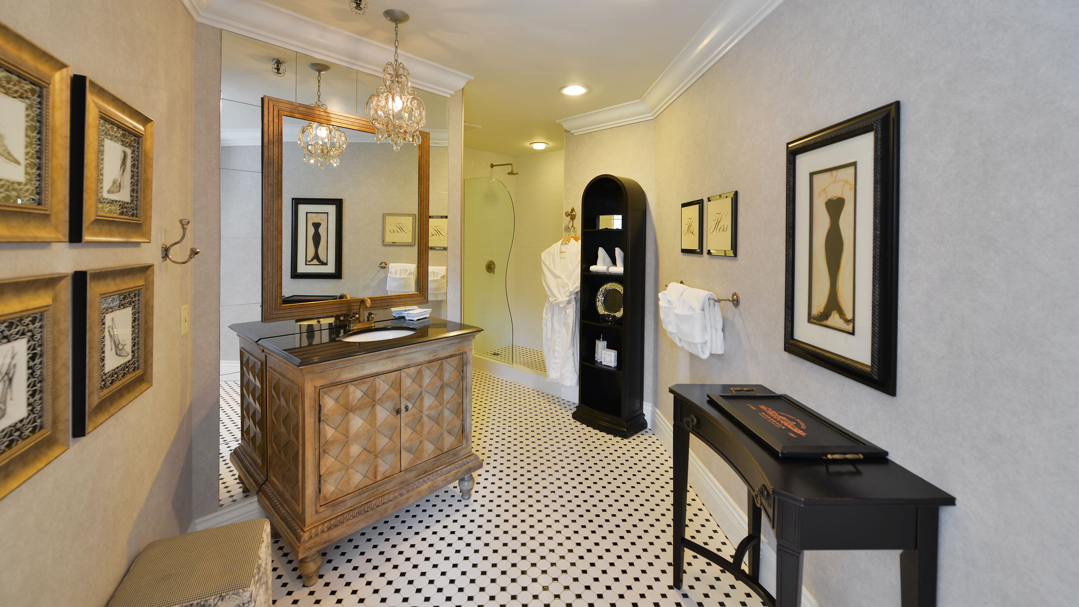 A bathroom with a vanity, mirror, chandelier, framed artwork, and a black console table.