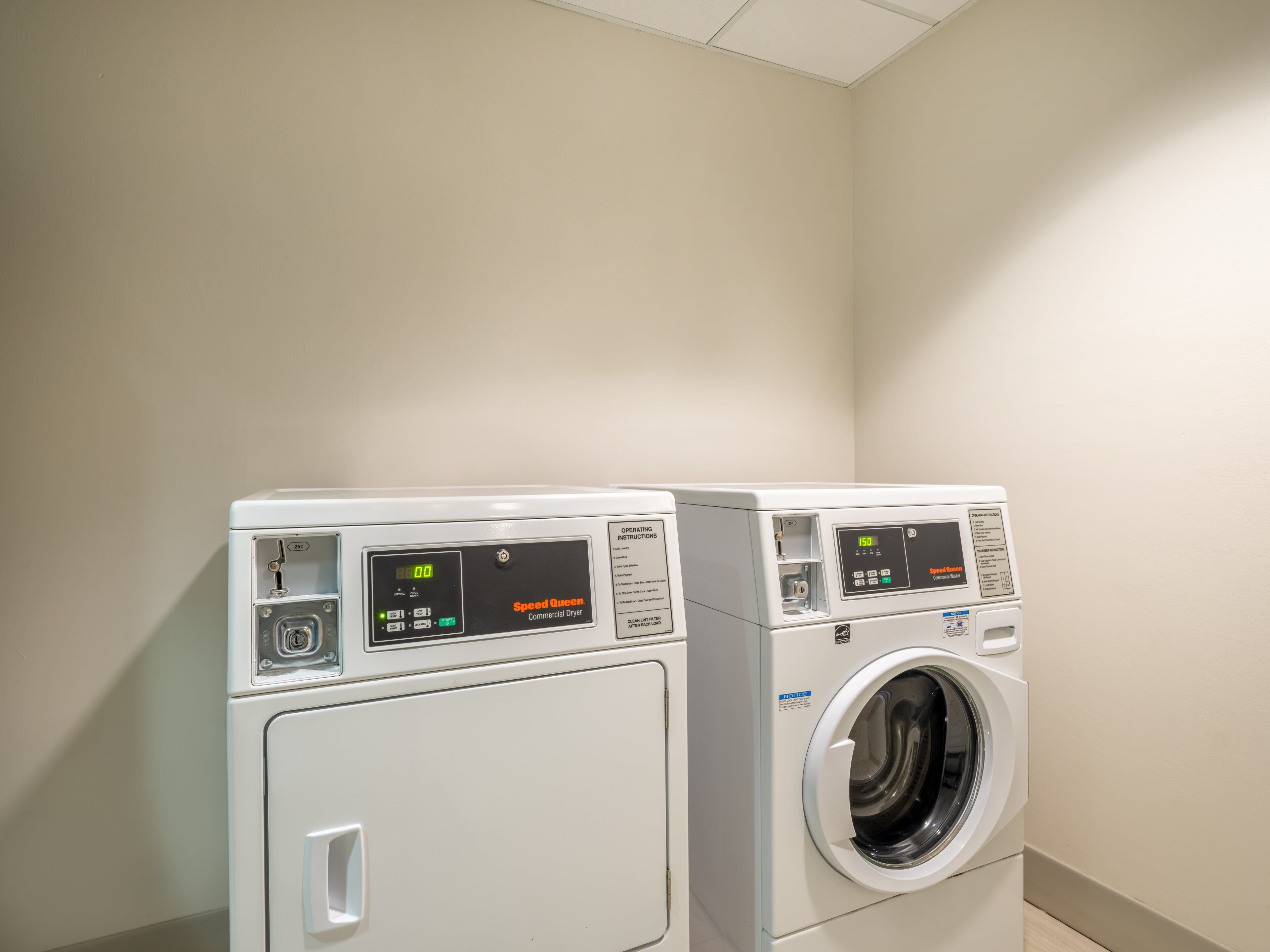 Two front-loading washing machines in a laundry room with a plain wall and a ceiling light fixture.