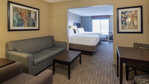 A hotel room with a gray sofa, a small table, a bed with white linens, a ceiling fan, and two framed artworks on the walls.