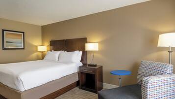 A hotel room with a large bed, two bedside lamps, a small round table, a patterned armchair, and a framed picture on the wall.