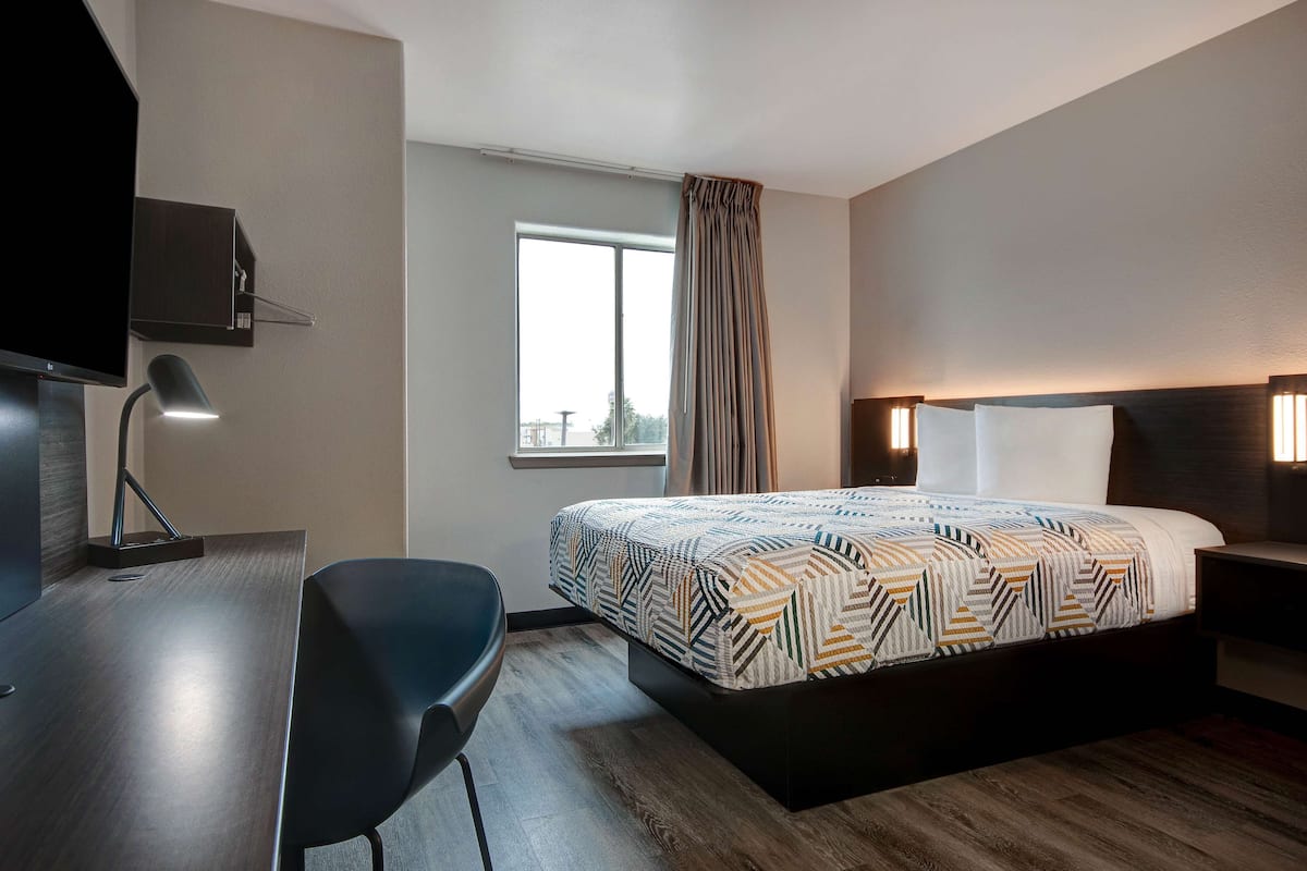A hotel room with a bed, a desk, a chair, a TV, a window, and a curtain.