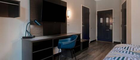 Una habitación de hotel con cama, escritorio, silla, televisor y puerta.
