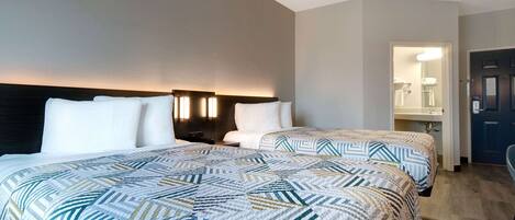 A hotel room with two beds, a nightstand, a mirror, and a door leading to a bathroom.