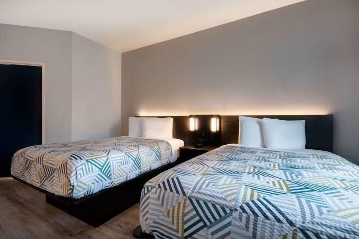 A hotel room with two beds, a dark door, and a wall-mounted light fixture.