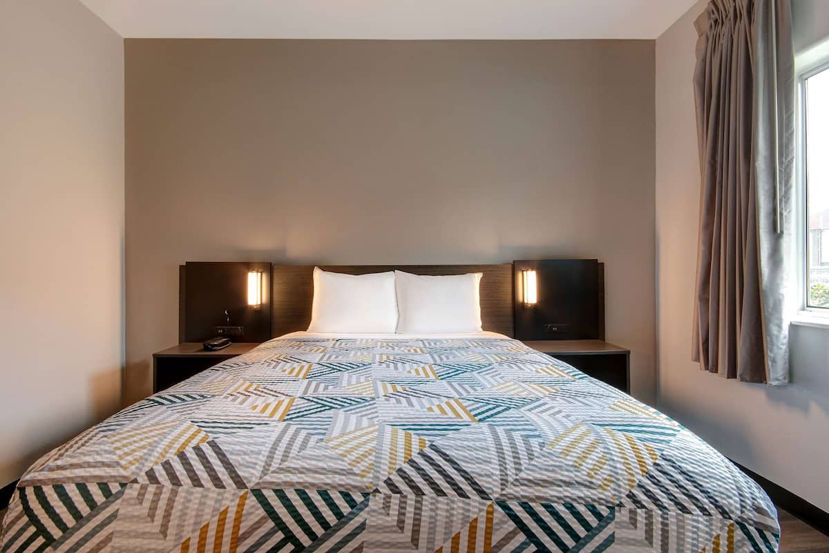 A hotel room with a large bed, two bedside tables, and a window with curtains.