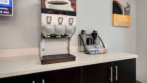 A coffee machine with three dispensers, a coffee cup display, and a coffee cup on the wall. - Motel 6 Pharr, TX (Pharr)
