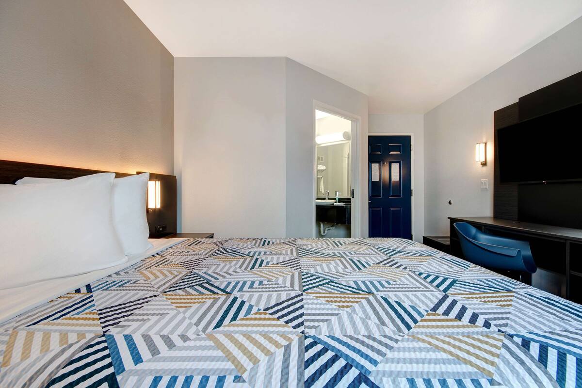 A hotel room with a large bed, a desk with a chair, a TV, and a door leading to a bathroom.