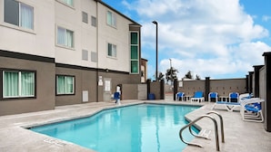 A swimming pool with blue water, surrounded by lounge chairs and a building with multiple windows and a door. - Motel 6 Pharr, TX (Pharr)