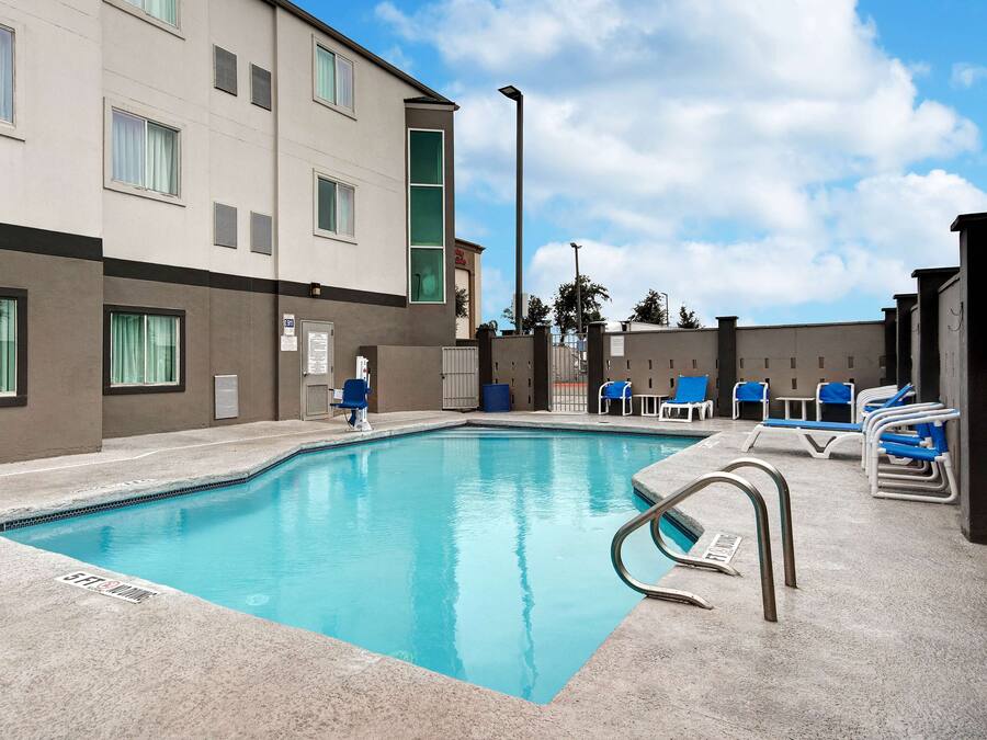 A swimming pool with blue water, surrounded by lounge chairs and a building with multiple windows and a door.