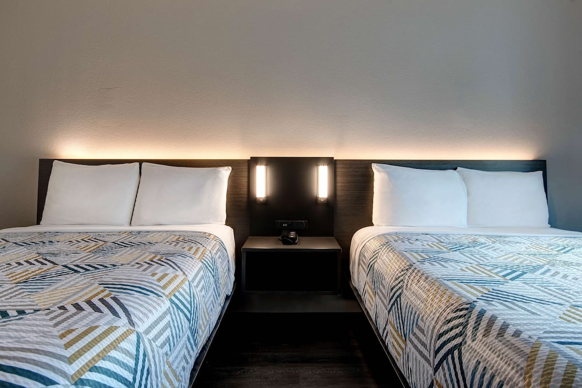 A hotel room with two beds, each with a patterned bedspread, a nightstand between them, and wall-mounted reading lights.