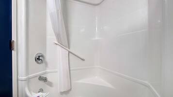 Esquina de un baño con una bañera blanca, una cortina de ducha y un asidero.