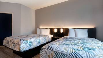 A hotel room with two beds, each with patterned bedding, bedside lamps, and a dark headboard.