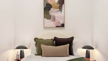 A bedroom with a bed, pillows, a blanket, two bedside tables with lamps, and a painting on the wall.