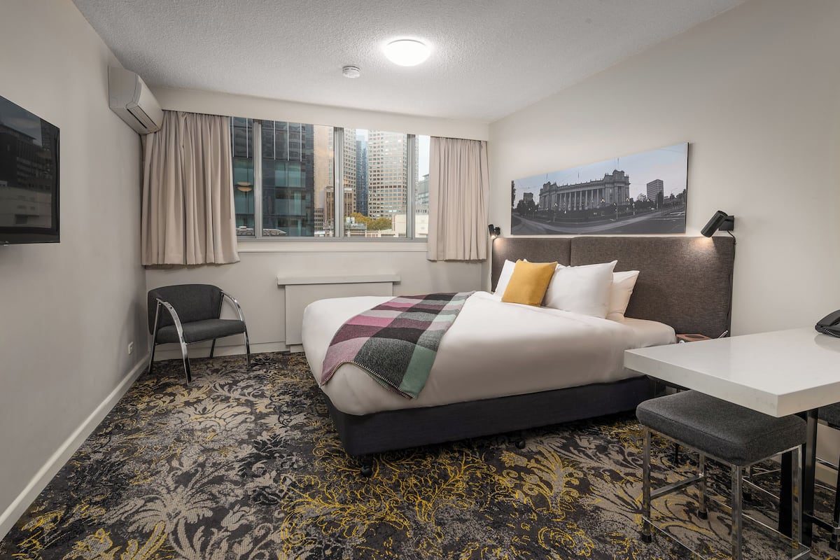 Habitación de hotel con una cama grande, un escritorio, una silla, una ventana con cortinas y vistas a la ciudad.