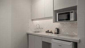 Una cocina moderna con armarios blancos, microondas integrado, un fregadero y un refrigerador pequeño.