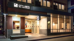Una entrada de hotel moderna con fachada de vidrio, un mostrador de recepción y un letrero que dice "CITY LIMITS HOTEL STUDIO APARTMENTS".