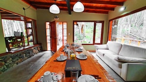 A dining area with a wooden table set for tea, a white sofa, and large windows with a forest view. - Patagonia Villa (Ushuaia)