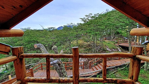 A wooden deck with a railing overlooking a forested area with a mountain in the background. - Patagonia Villa (Ushuaia)