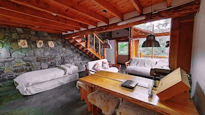 Une pièce rustique avec un mur en pierre, des poutres en bois au plafond, un escalier en bois, un canapé, une table et un banc.