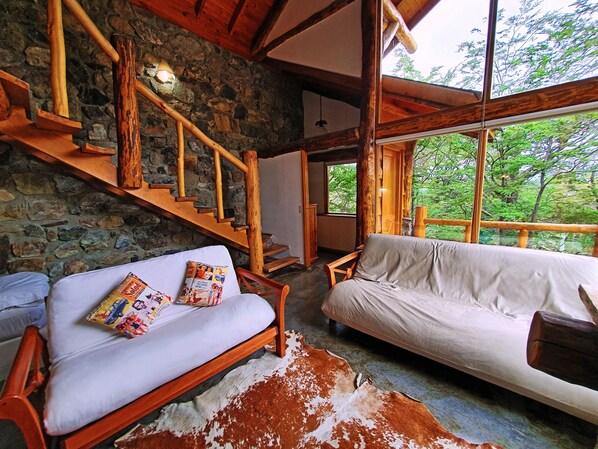 A rustic cabin interior with a stone wall, wooden staircase, two sofas, and a cowhide rug. - Patagonia Villa (Ushuaia)