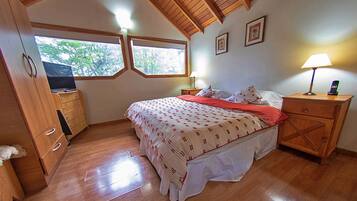 A bedroom with a bed, wooden dresser, nightstands, and a window with a view of trees.