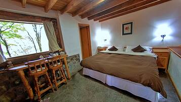 Un dormitorio con cama de madera, un escritorio con sillas, una pared de piedra y una ventana con cortinas.